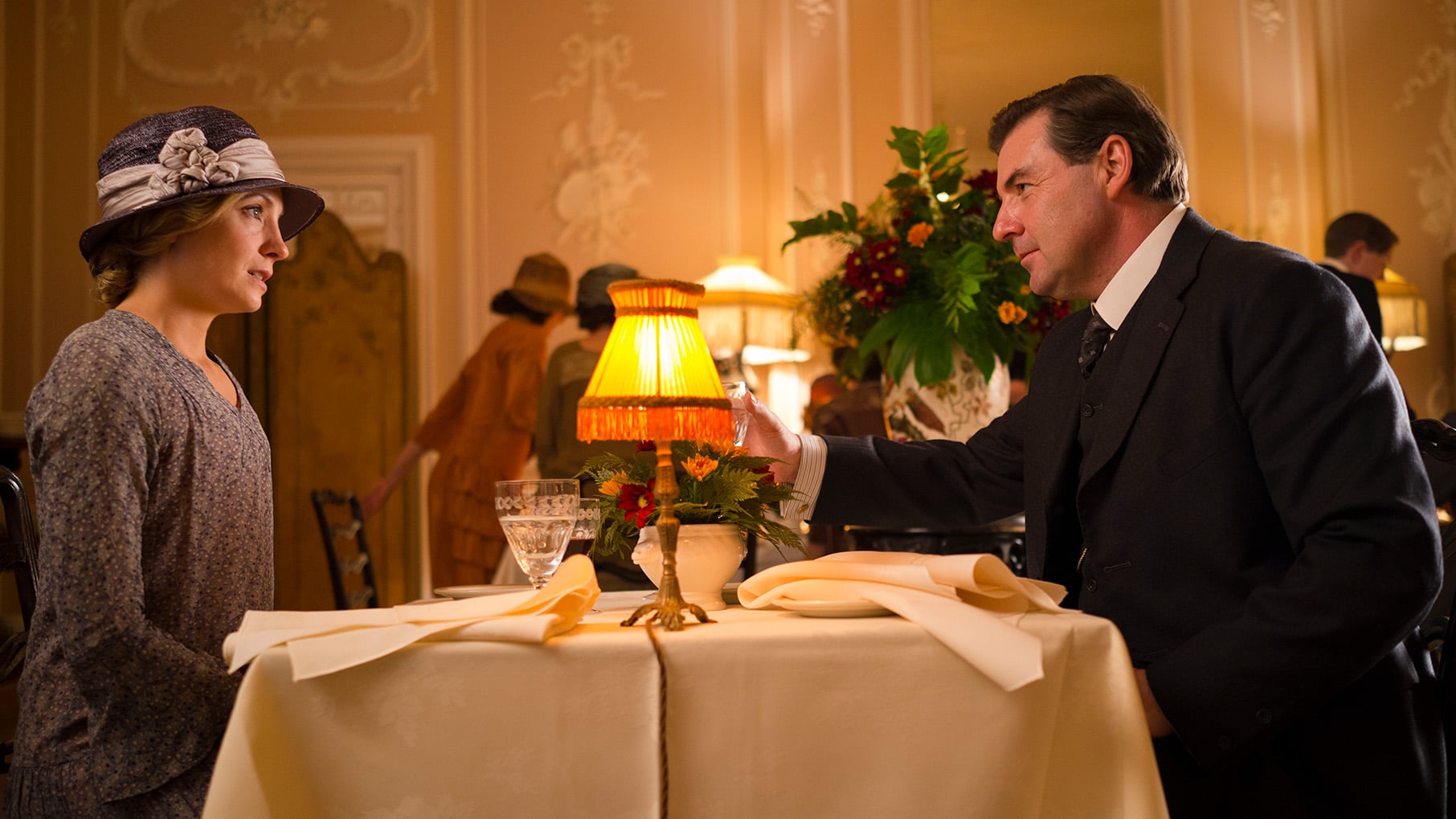 Anna sits across a table from Bates in a restaurant