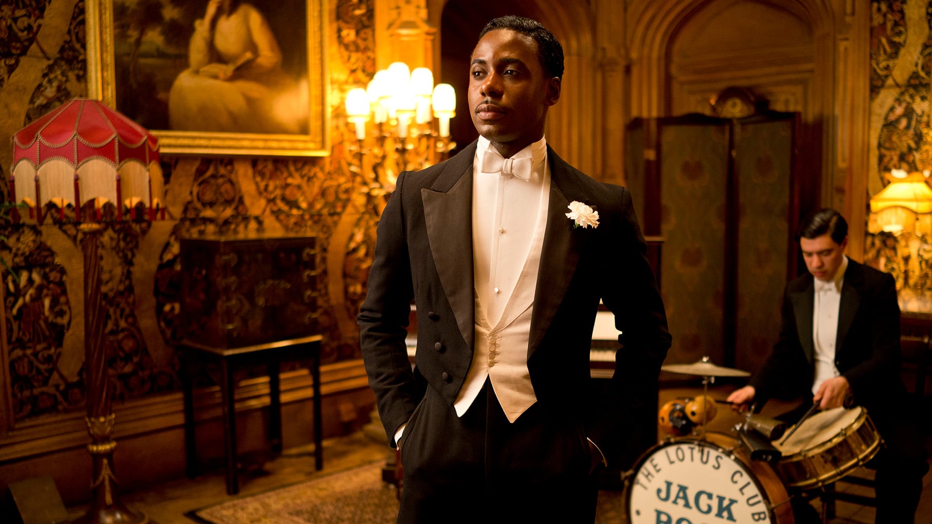 Jack Ross stands in a tuxedo in a nice room in front of a man sitting at a small drum set