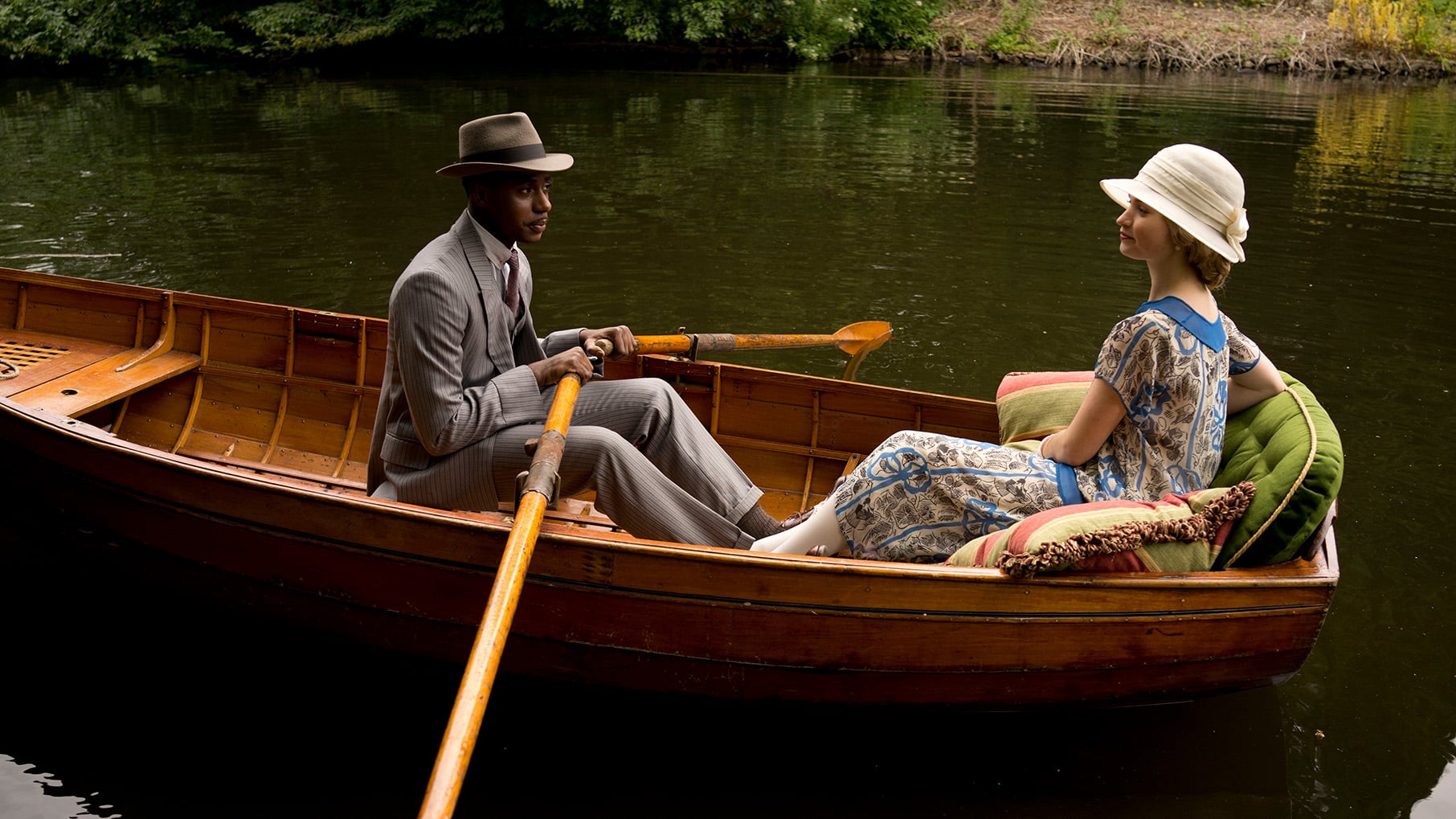 Jack Ross holds oars while sitting in a boat in a river across from Rose