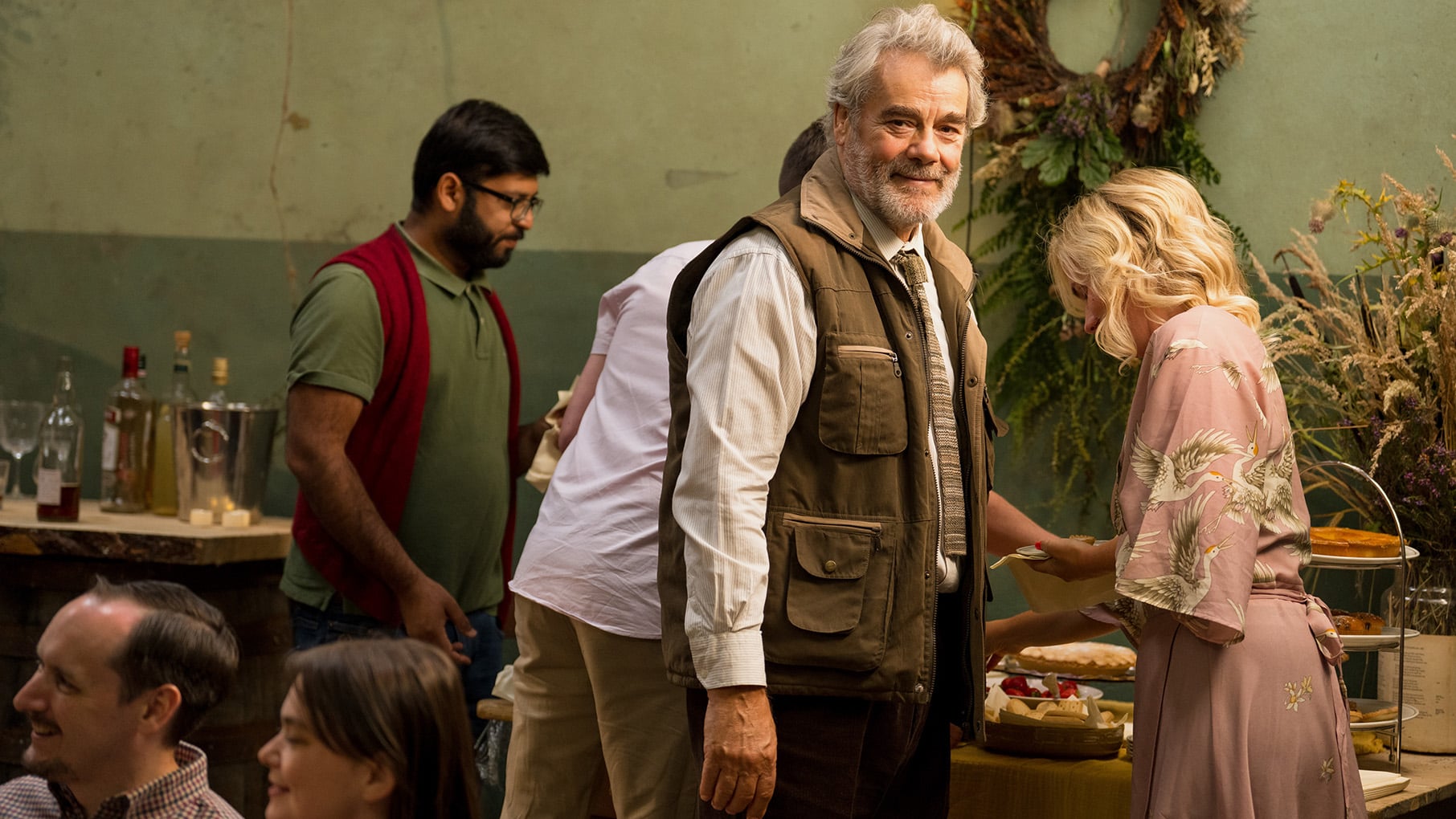 Angus stands in a vest with many pockets amongst a crowd serving themselves food and drink