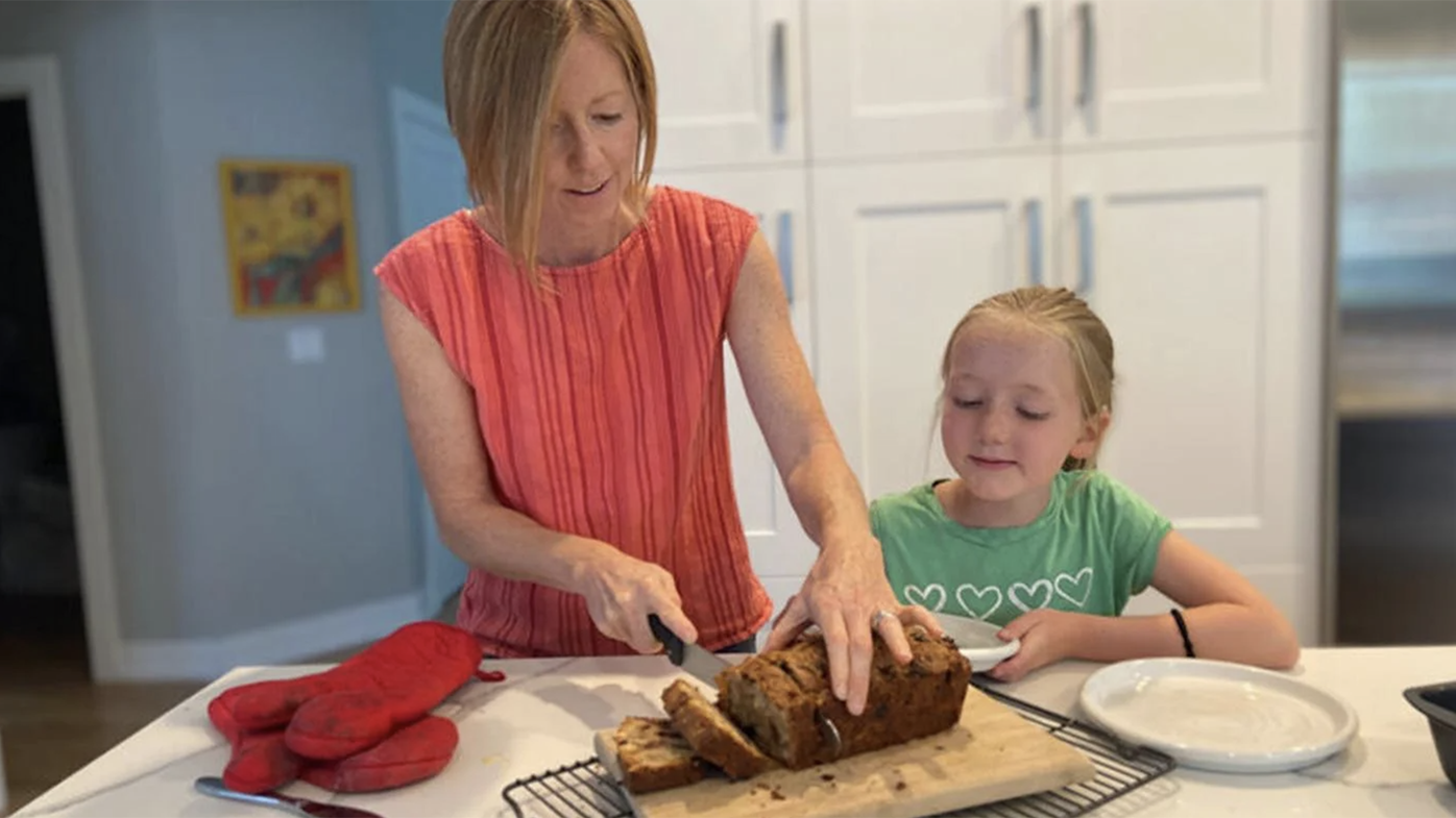 A woman slicing through a loaf of fruitcake while a girl looks on 