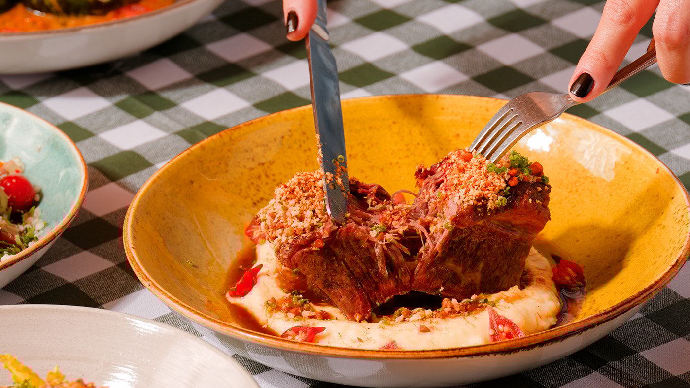Hands cut a short rib on a plate