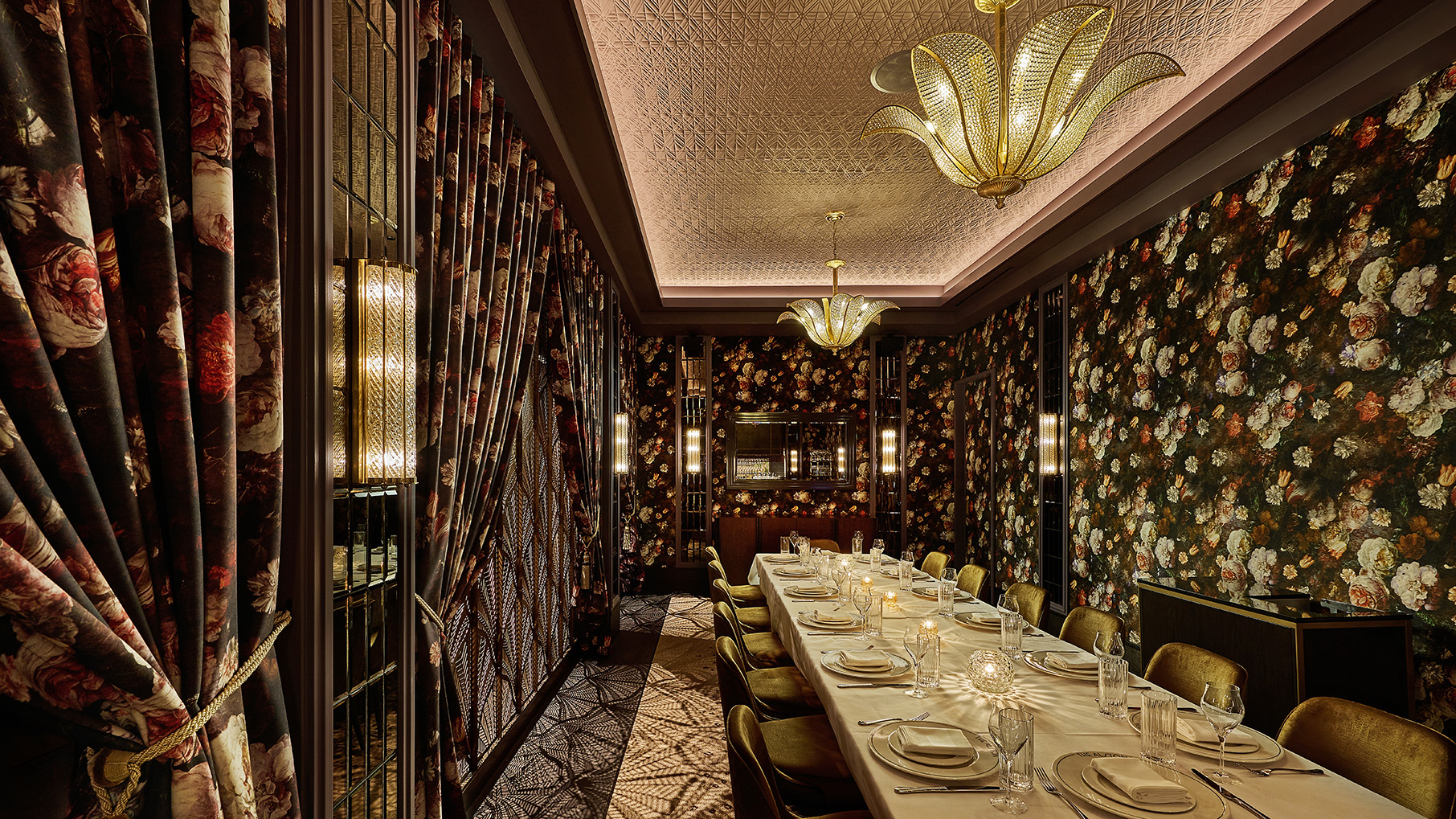 A long dining table in a room with floral wallpaper, curtains, and light fixtures