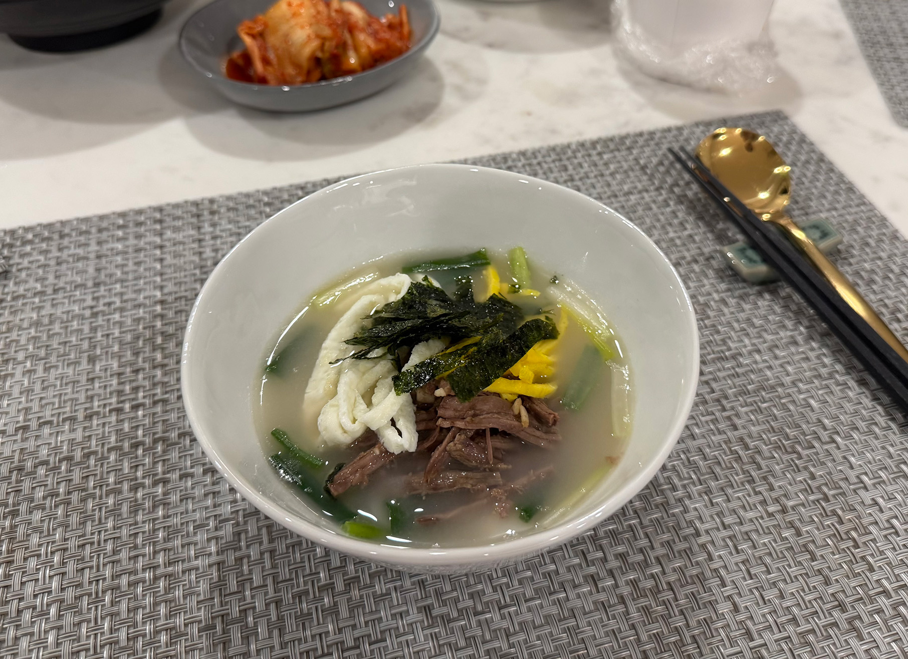 A bowl of soup next to a dish of kimchi
