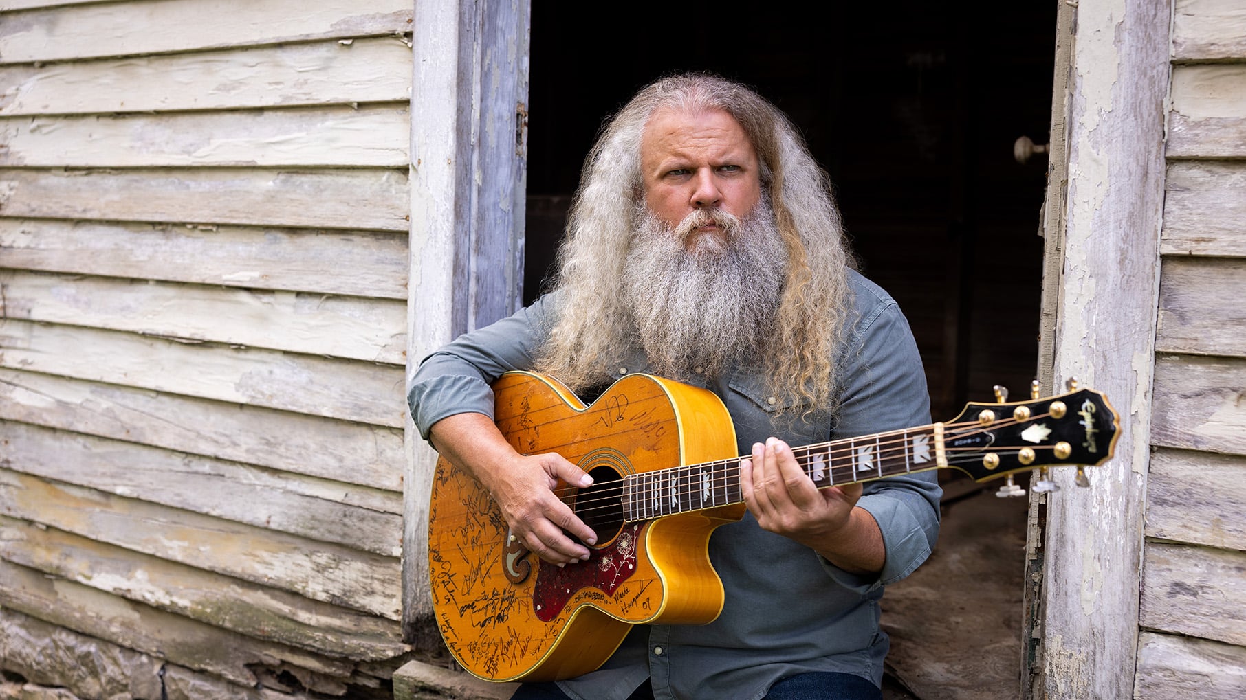 Jamey Johnson sits in the open door of a dilapidated shack with a guitar