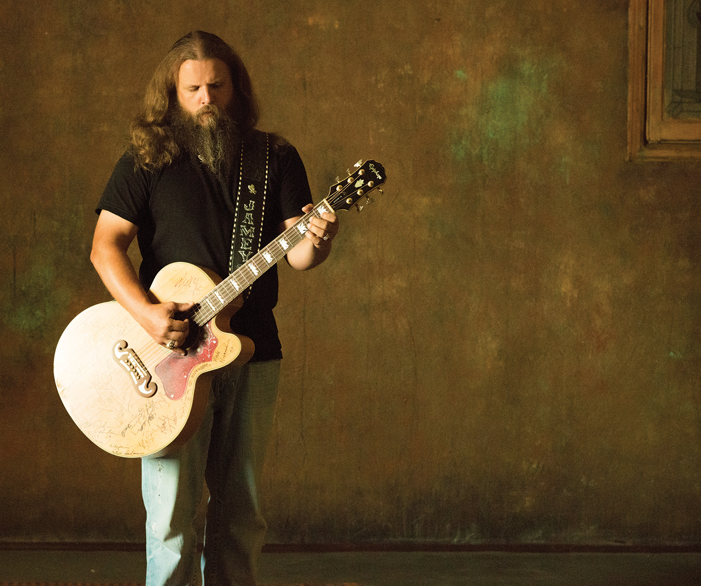 Jamey Johnson against a blank wall with a guitar