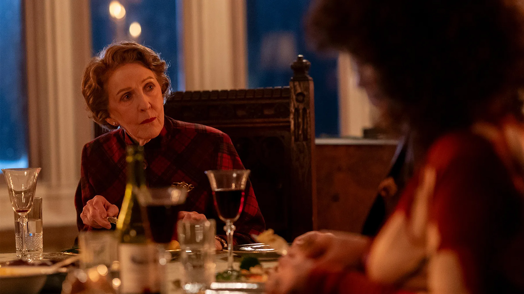 Patricia Hodge bends forward in her chair while sitting at a dinner table