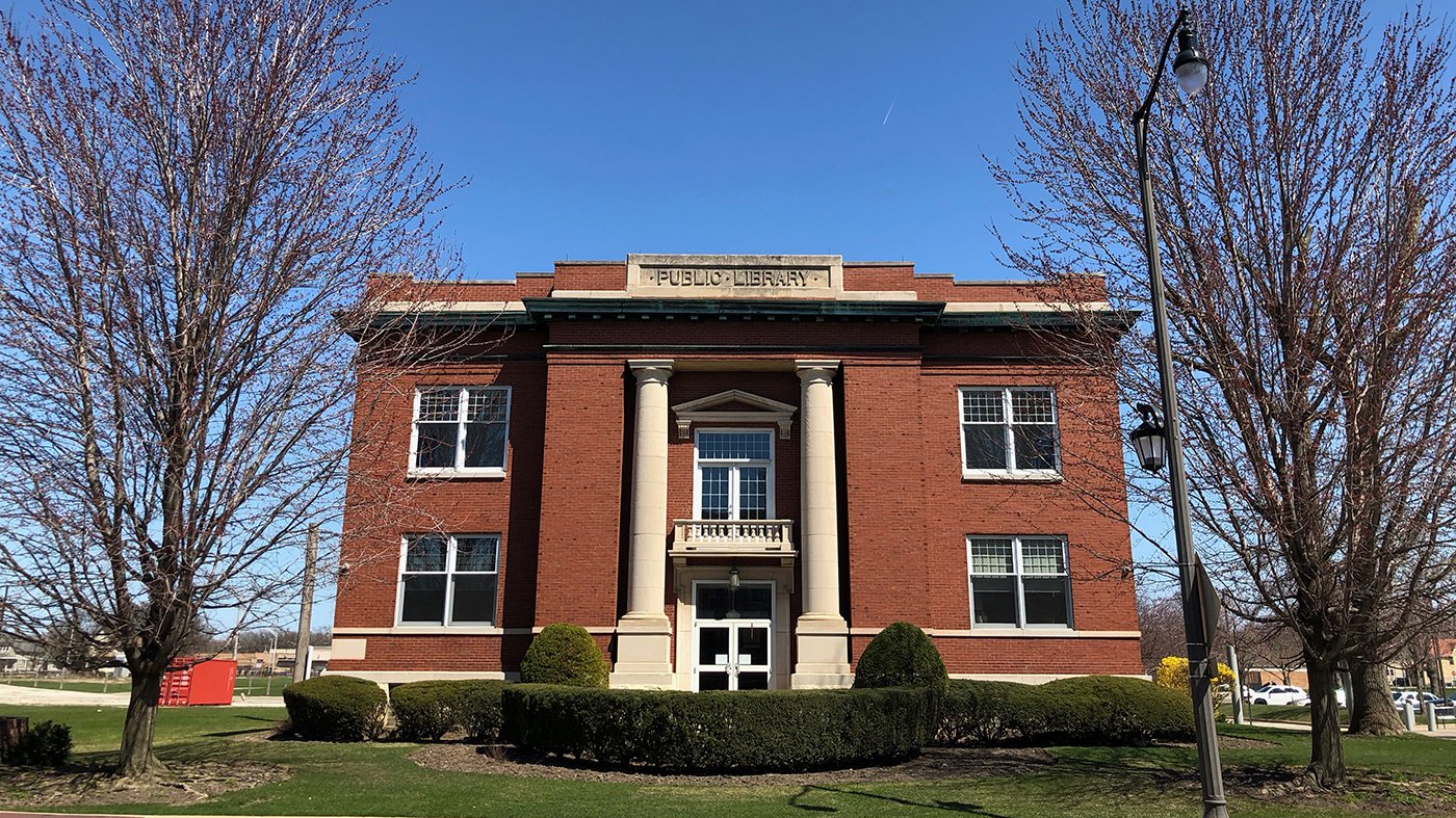 The Maywood public library between two trees, against a blue sky