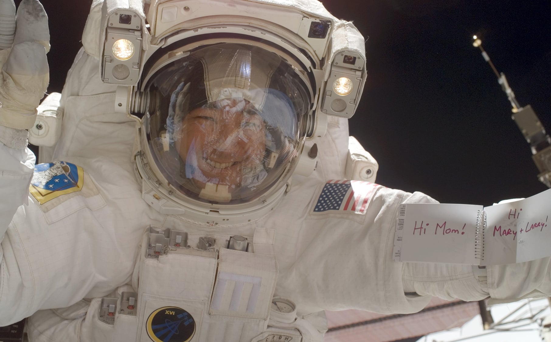 Dan Tani holding up a sign reading "Hi Mom" on a spacewalk