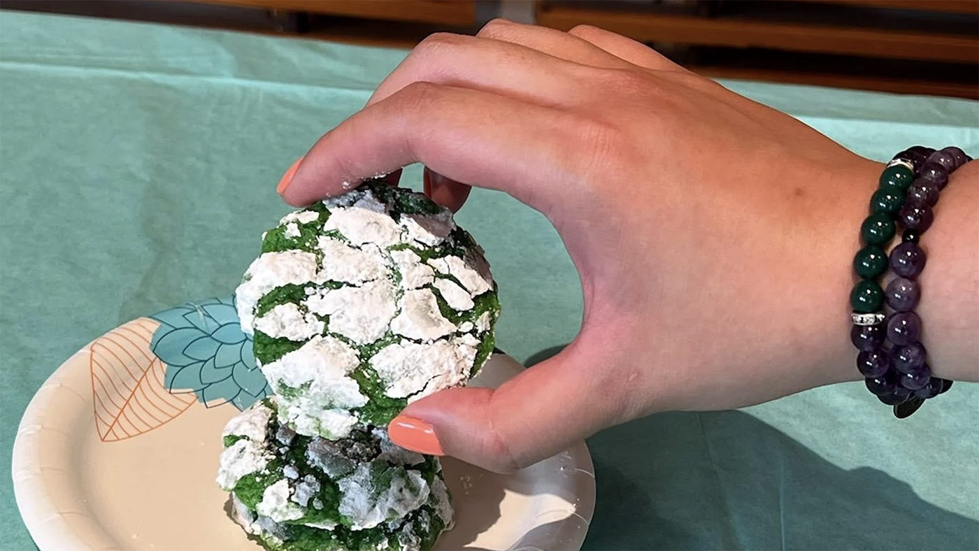 A hand lifting one of two green and white pandan crinkle cookies off of a plate