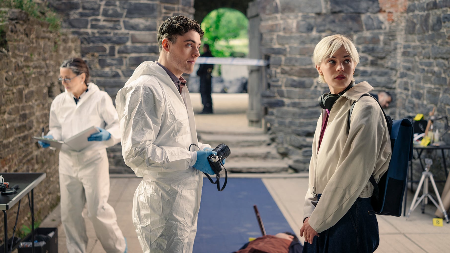 Patience, Elliot, and Dr. Parsons stand in an old castle around a body