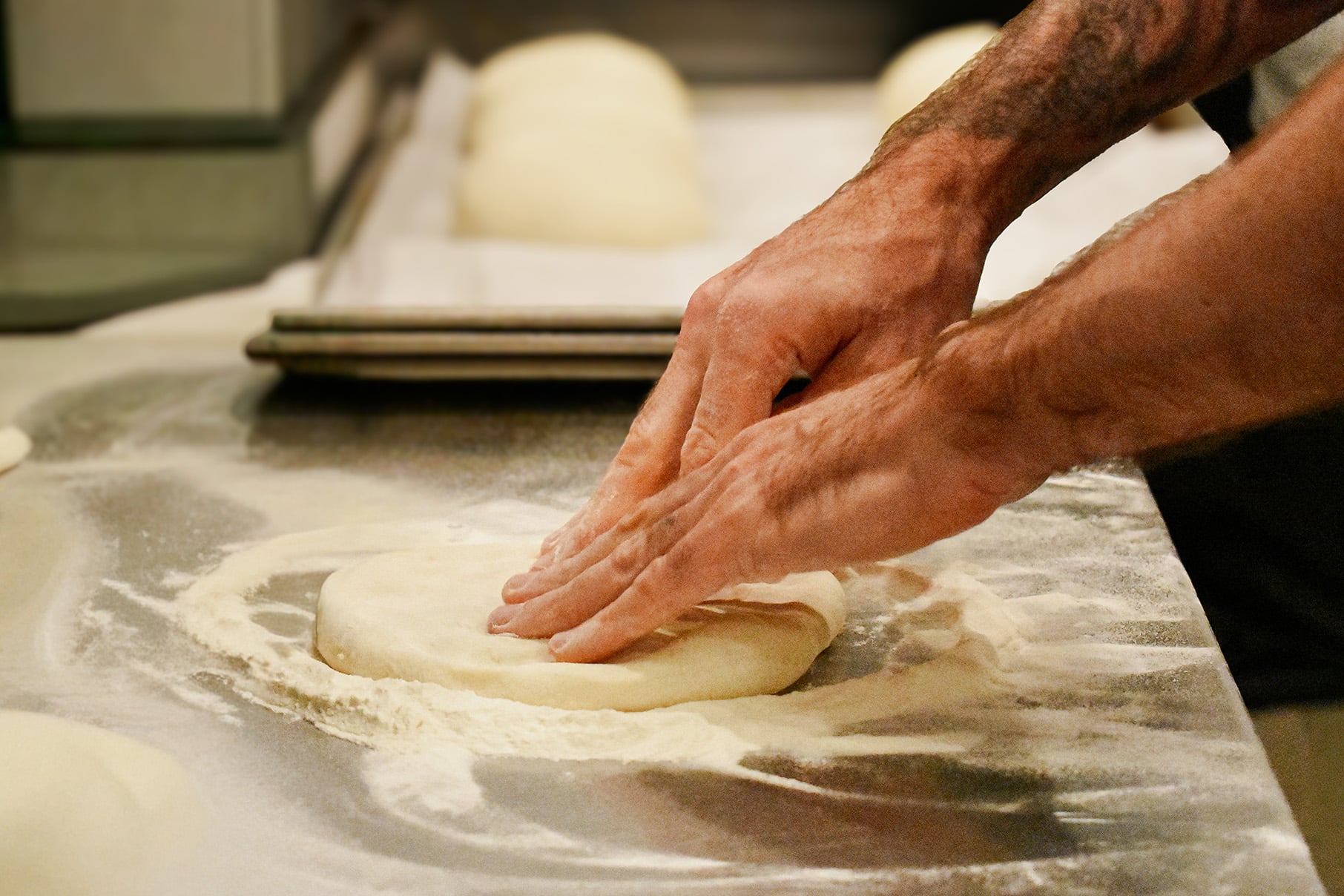 Hands press dough into a circle on a floured surface