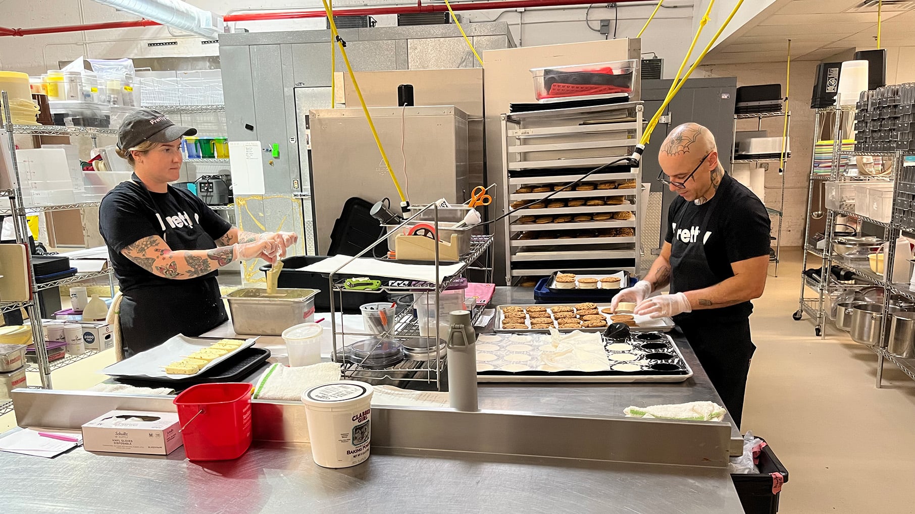 Someone dips ice cream bars into a coating across from someone making ice cream sandwiches