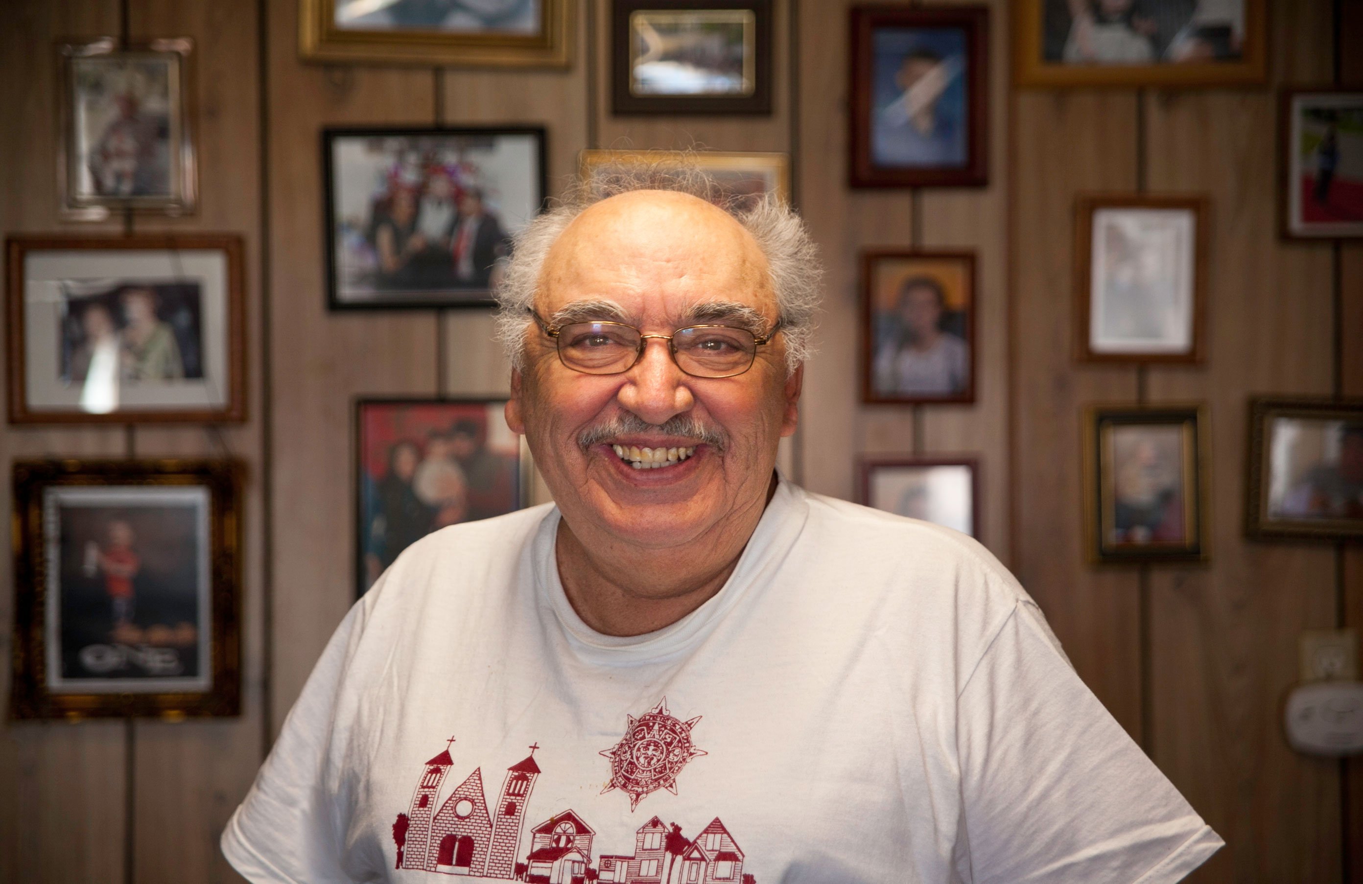 Raul Hernandez stands in front of his living room wall covered in family photos.