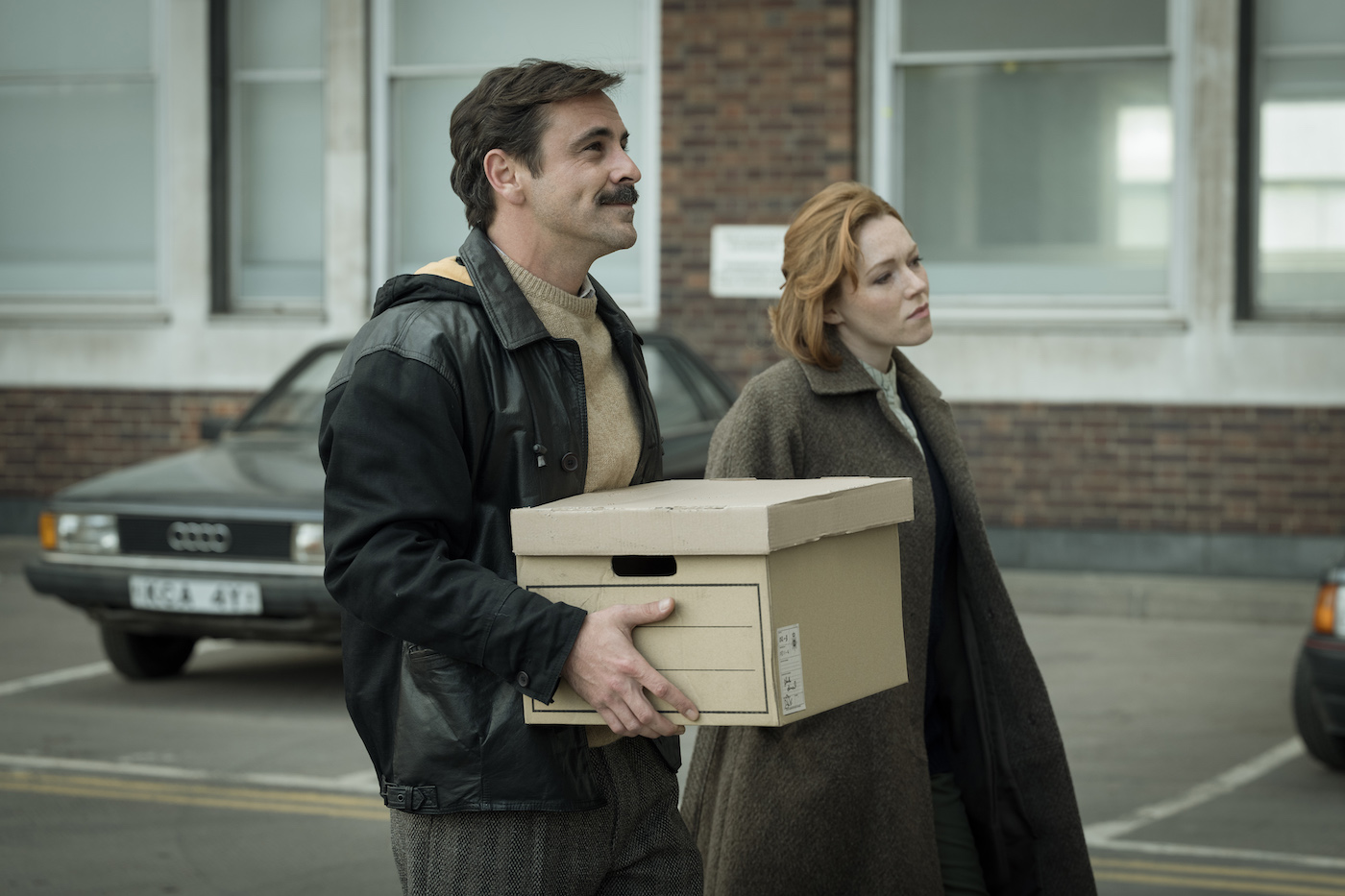 A man carries a cardboard box outside next to a woman