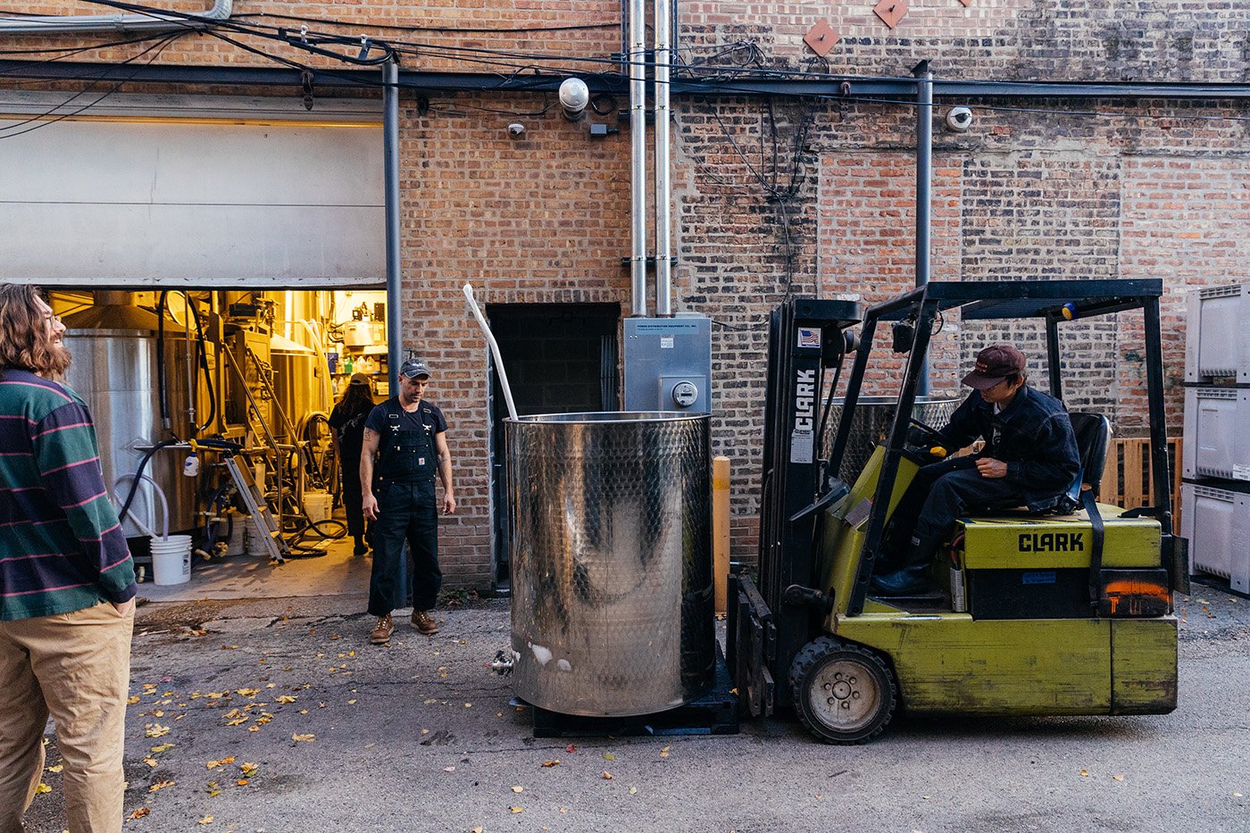 A forklift with a stainless steel vat on it in an alley