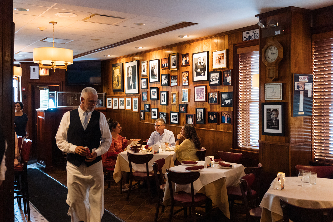 A server walks through a restaurant with a wall full of photos