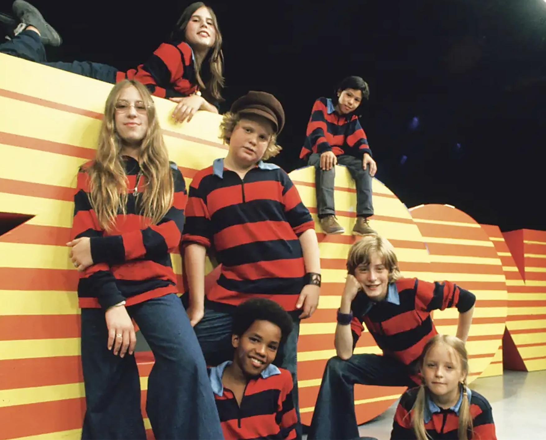 Children in the cast of Zoom against yellow and orange Zoom backdrop