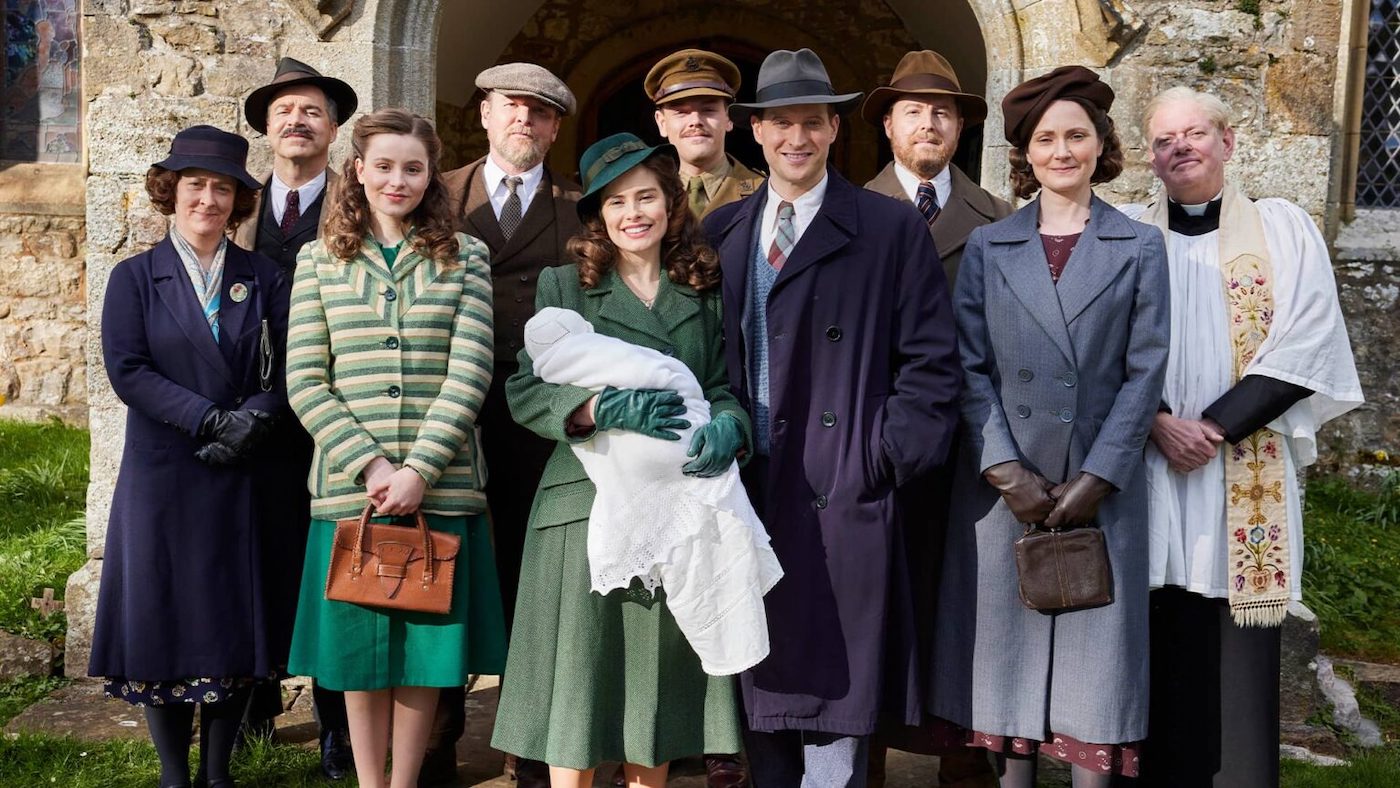 A portion of the cast of All Creatures Great and Small poses for a photo in front of a church