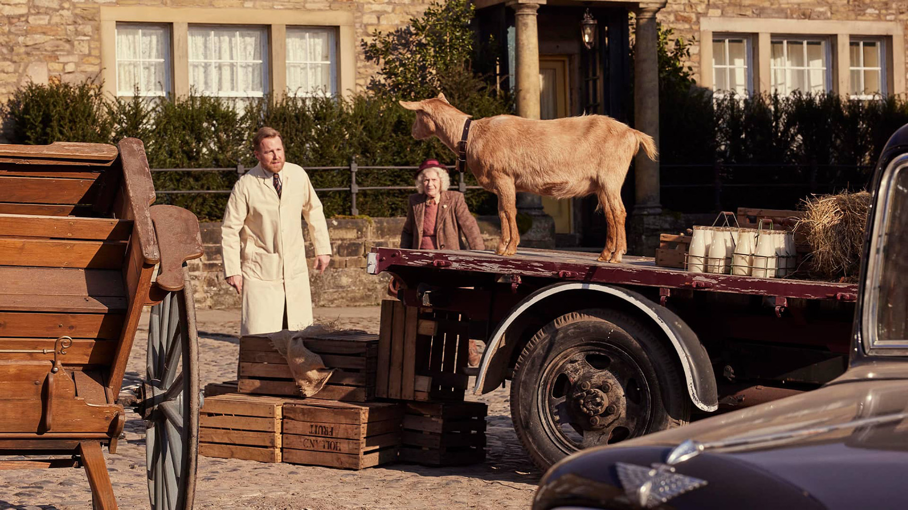 Siegfried and an older woman look at a goat on a flatbed trailer