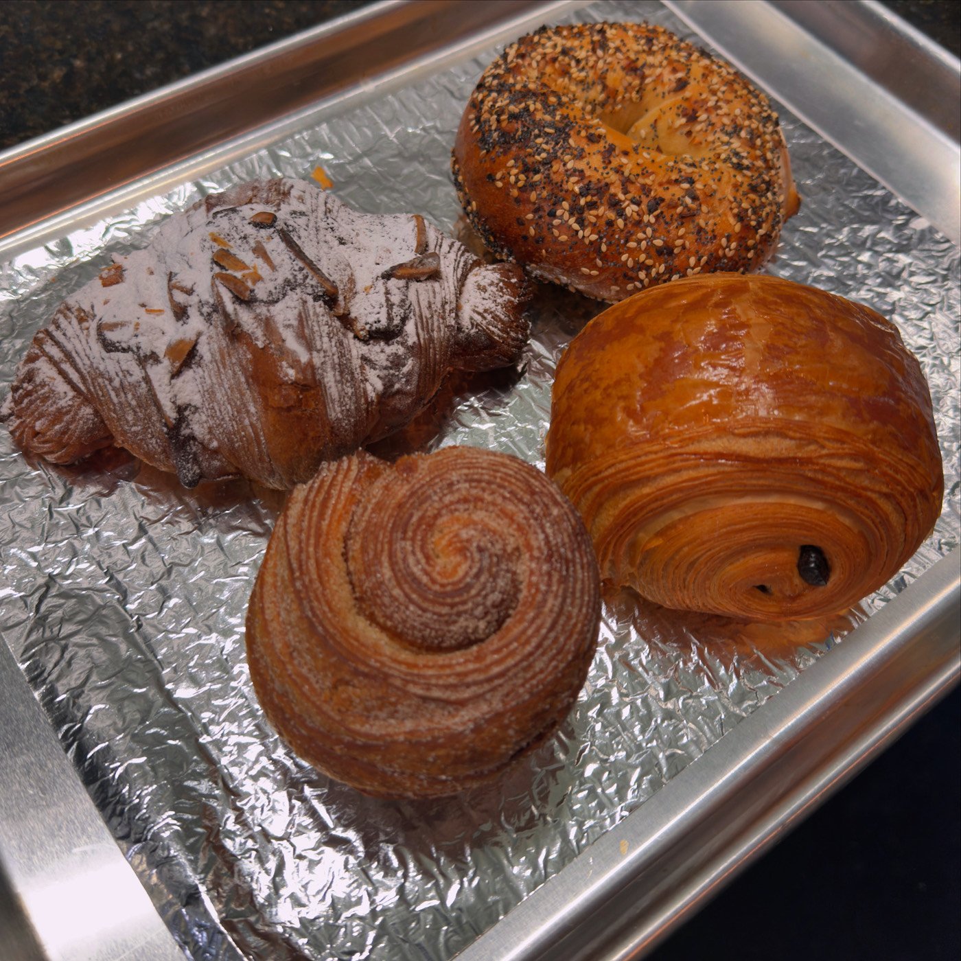 Three croissants and a bagel on a foil-lined pan