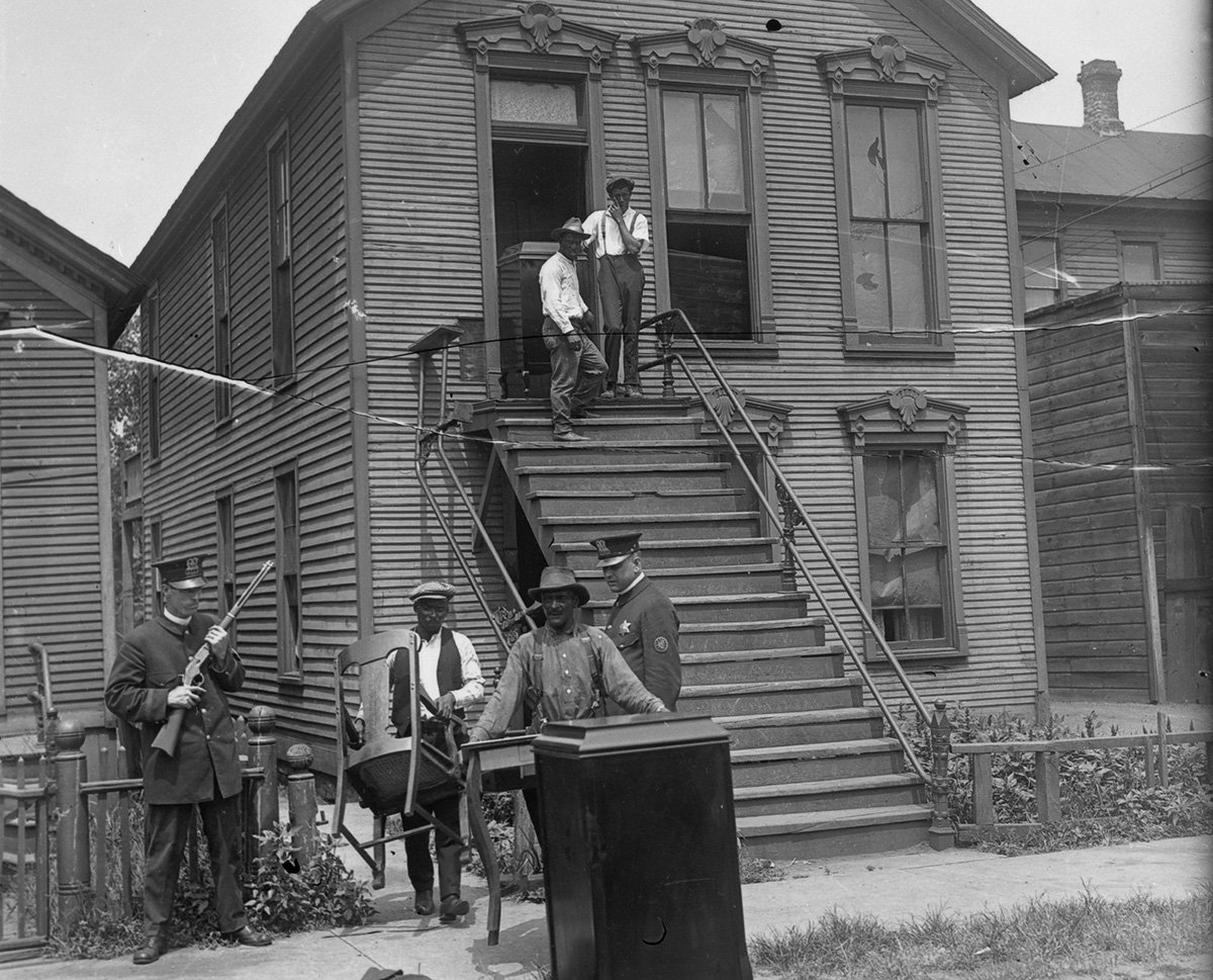 People moving from house, accompanied by policemen during race riots