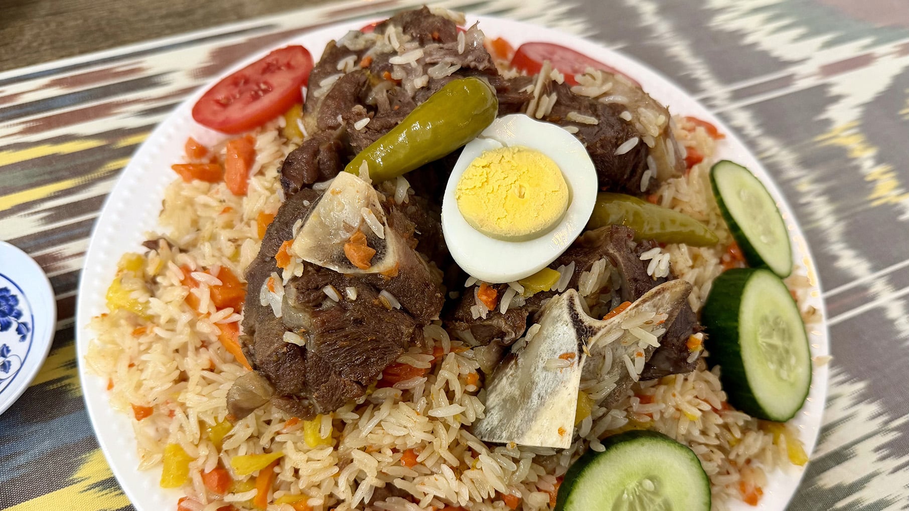 A plate with rice topped with shanks of meet, boiled egg, vegetables, and more