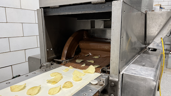 Potato chips on a conveyor belt going through a curtain of liquid chocolate 