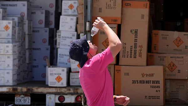 Wyatt Seymore pours the last drops of liquid from a water bottle into his mouth as he takes a break from unloading a stiflingly hot trailer of fireworks outside Powder Monkey Fireworks ahead of the opening of the stand, June 17, 2024, in Weldon Spring, Mo. Credit: AP Photo / Jeff Roberson, File A man in a hat and pink shirt pours water from a plastic bottle into his mouth in front of boxes
