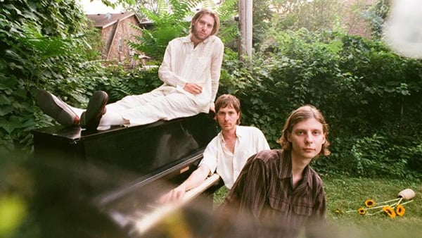 Three men sit on or near a piano