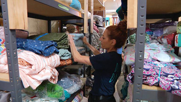 Credit: WTTW News A woman sorting through blankets on storage shelves