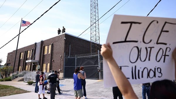 The Broadview ICE facility with a protester holding up a sign, "ICE OUT OF ILLINOIS" in the foreground.