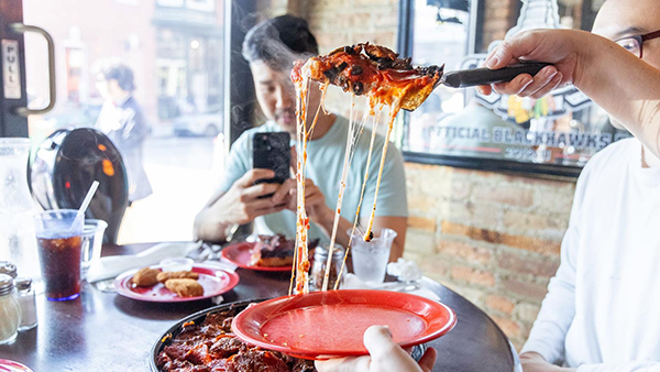Pequod’s Pizza has been named the best pizza in America on Yelp and appeared on 'The Bear,' and continues to draw both tourists and locals for its Chicago-style pizza. Credit: Kathleen Hinkel for WTTW A slice of pizza is lifted to a plate as someone films with a phone