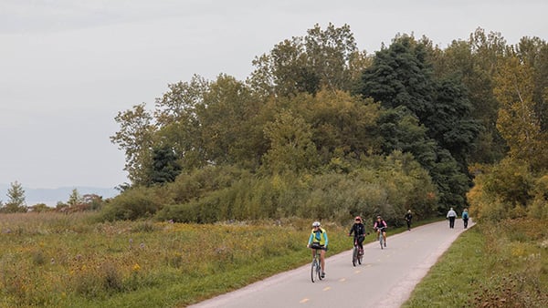 The Island Line Trail in Burlington, Vermont. Credit: Oliver Parini People ride bikes down a paved trail among grass and trees