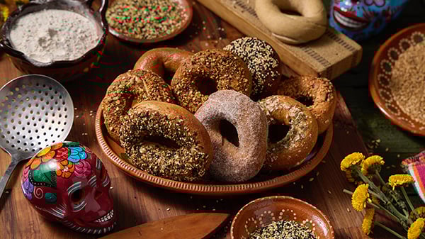 Felix Zepeda incorporates his Mexican heritage into the sourdough bagels he sells under Rosca, with flavors like red mole. Credit: Provided Bagels on a dish next to a Mexican skull, cream cheese, and more on a table