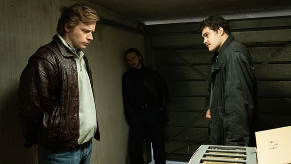 Three men stand in a garage with gold bars