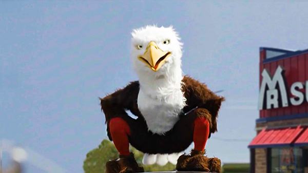 A person in an eagle costume on top of a car in front of a blue sky