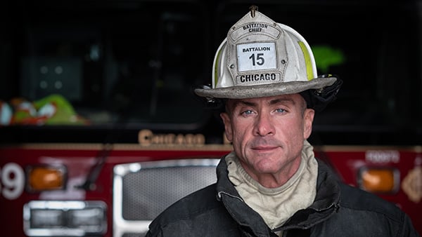 A firefighter wearing his helmet stands in front of a fire truck