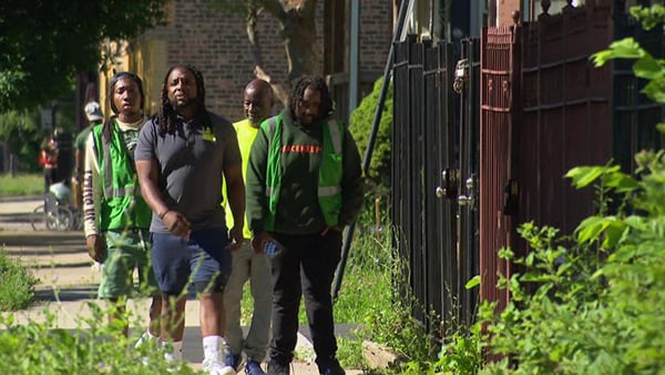 A group of men from a violence intervention group wearing reflective vests walking down a Chicago sidewalk