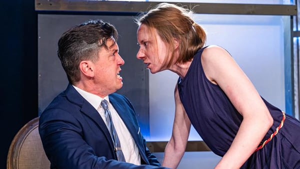 A man sitting in a chair and a woman leaning toward him exchange words