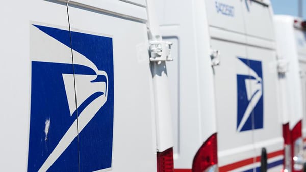 A row of US Postal Service trucks lined up in a parking lot
