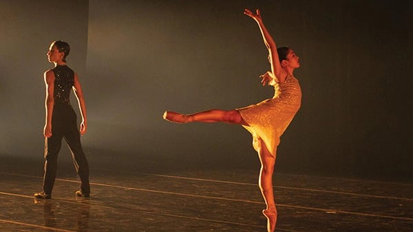 A ballerina hits a pose while another dancer stands facing away behind her on a stage