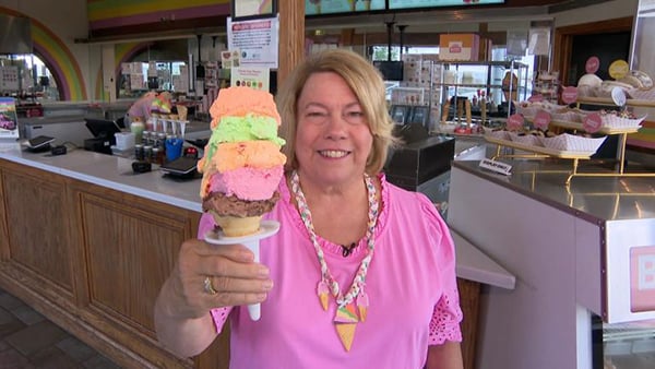 Original Rainbow Cone owner Lynn Sapp holds up a large rainbow cone while smiling at the camera