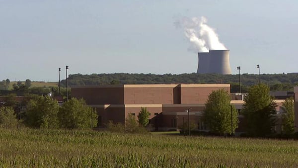 A field and building in the foreground with nuclear cooling towers in the background