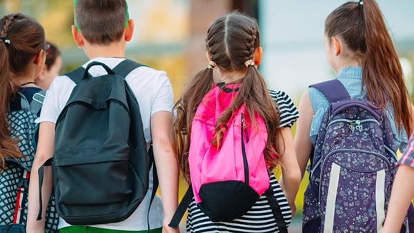 A stock image of four elementary age children wearing backpacks and walking away from the camera