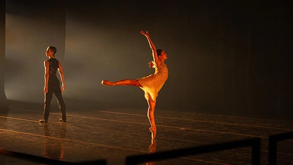 A ballerina on a shadowy stage with another dancer facing away from her