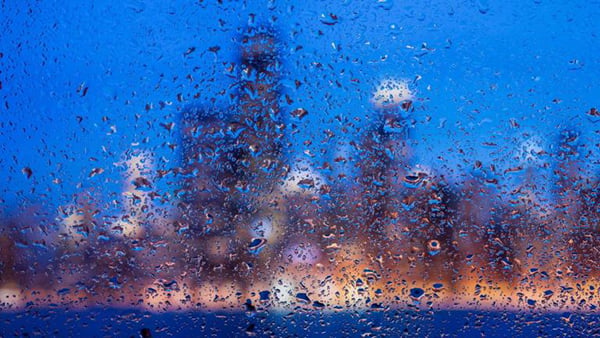 The outline of the Chicago skyline at dusk is blurred behind a rainy window