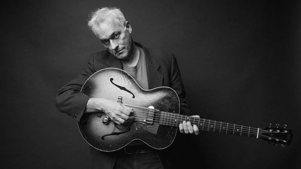 Marc Ribot poses with his guitar in a black and white image