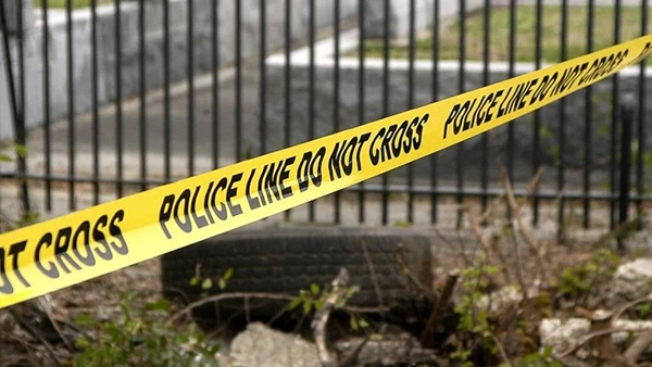 Police caution tape in the foreground, with a tire and fence in the background