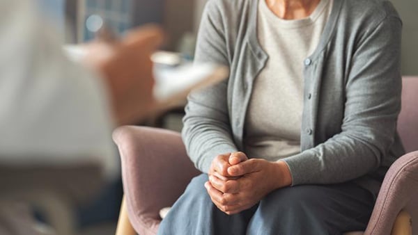 A stock image of a woman, visible from the shoulders down, seated with her hands clasped